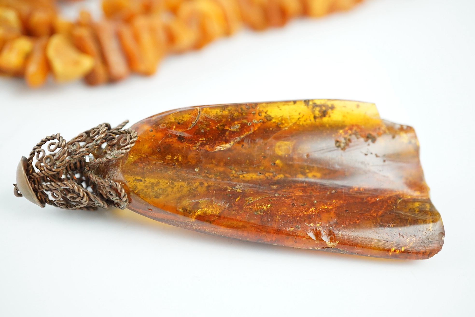 A long single strand unpolished amber necklace, 162cm and a gilt metal mounted amber pendant, gross weight 205 grams. Condition - fair